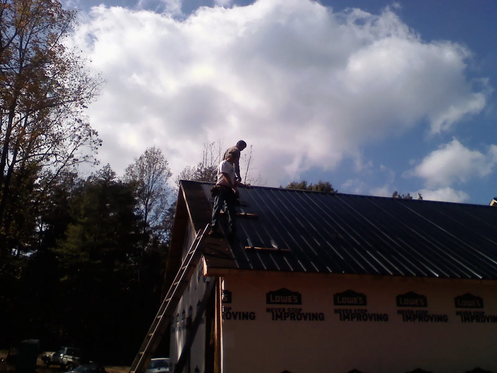 Roofer fastening dark metal panels high against a cloudy sky, from a Roof Inspection job in Corfu