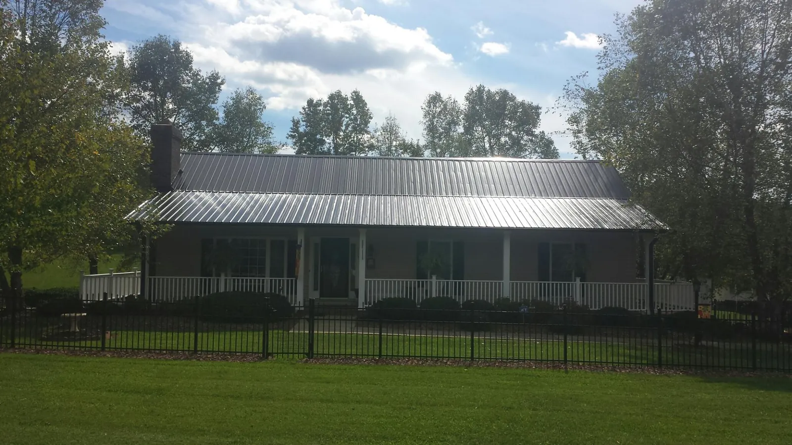Gray metal roof on a brick ranch with a full width front porch — Gutter Guard Installation work by our crew in Corfu