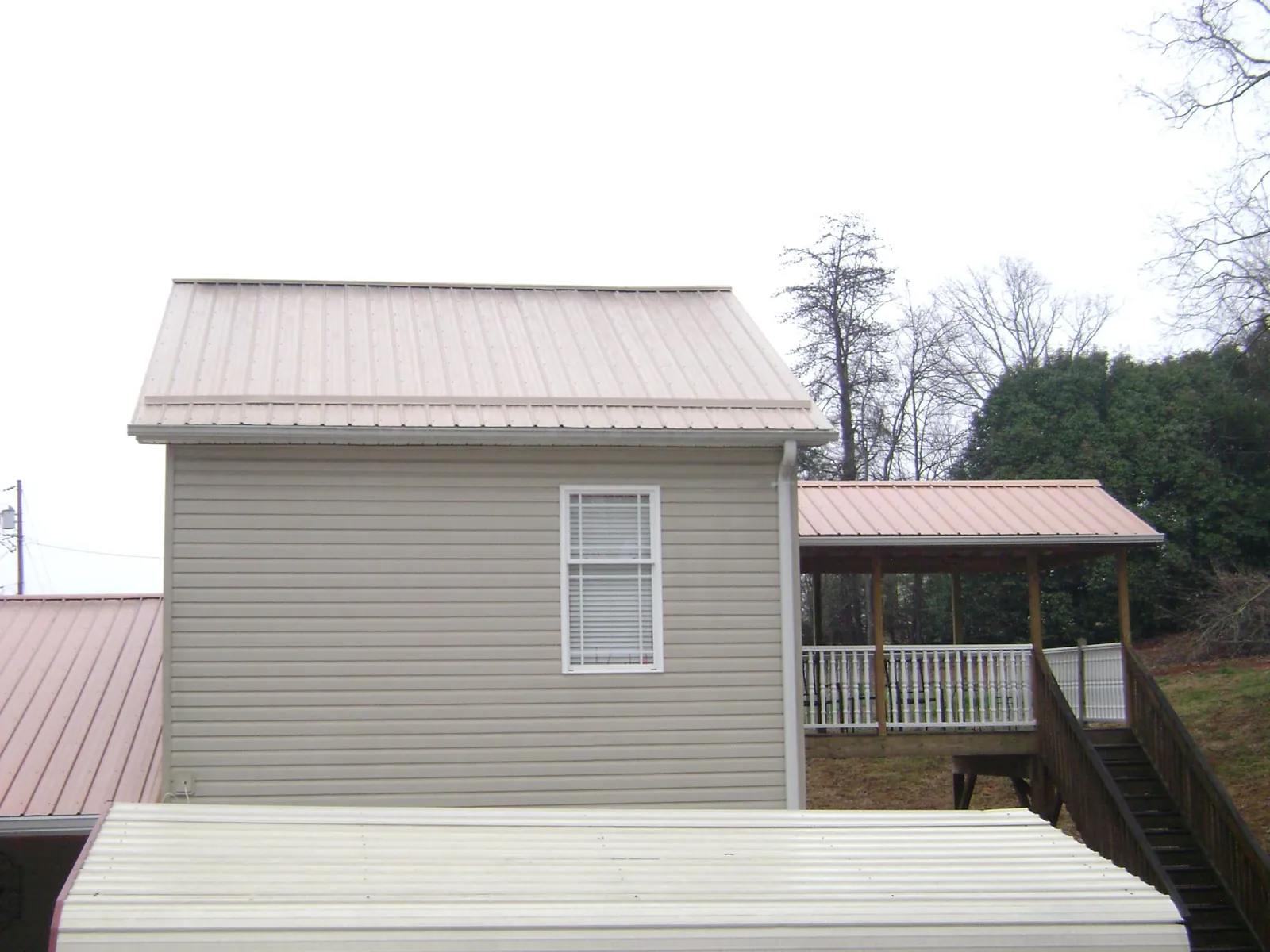 Tan metal roofs on a two story addition and attached porch, from a Roof Replacement job in Corfu
